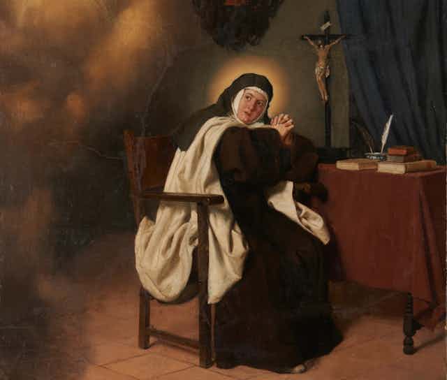 Una monja con hábito reza delante de una mesa y un crucifijo.