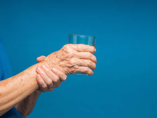 Older person holding a glass of water with one hand and their wrist with the other