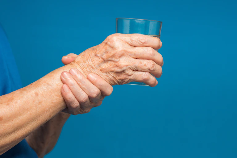 Older person holding a glass of water with one hand and their wrist with the other