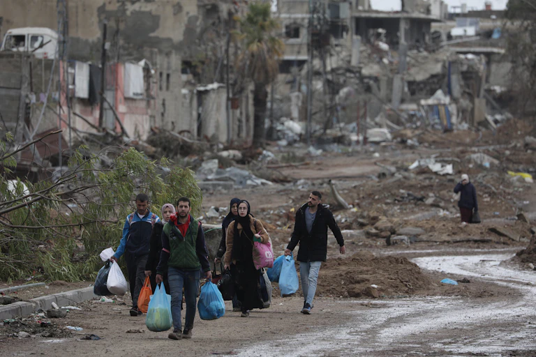 Men and women with carrier bags, walk along past bombed out buildings