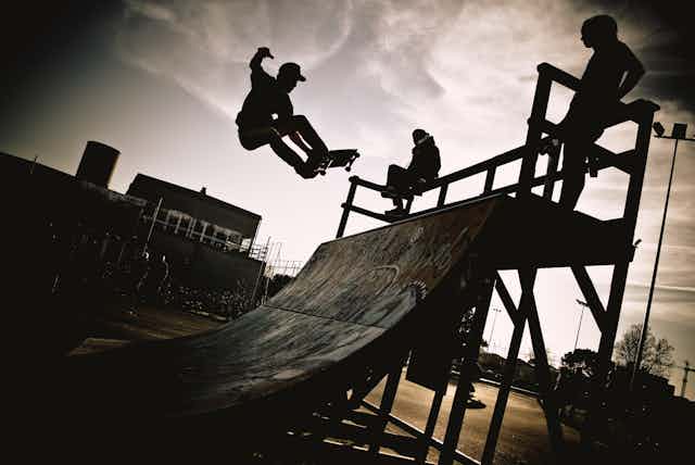 Three skateboarders silhouetted against the sky in black and white.