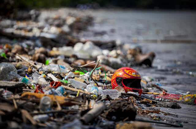 Plastic bottles, wrappers and a motorcycle helmet on a trash-strewn beach.