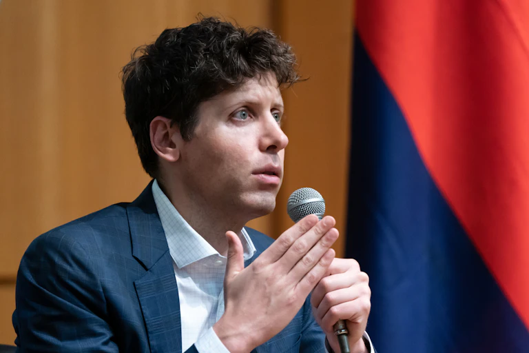 Man in a blue suit jacket, white shirt and no tie speaks while holding a microphone.