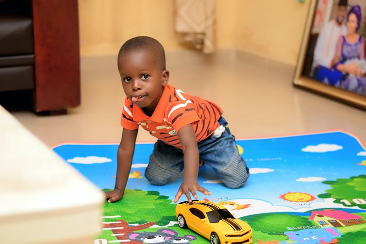 A young Black boy pushes a car along a colorful playmat