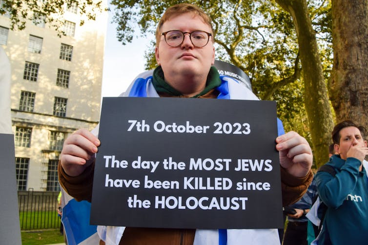 Un hombre afuera sosteniendo un cartel que dice que el 7 de octubre fue el día en que más judíos fueron asesinados desde el Holocausto.