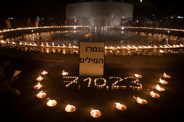 Candles lit around a reflecting pool and a sign in Hebrew that says 'No more words.'