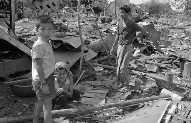 A boy looks into the camera as he stands in rubble