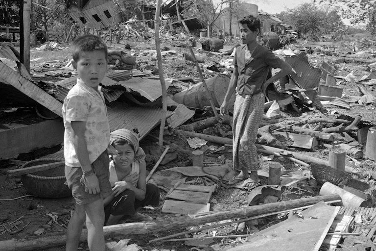 A boy looks into the camera as he stands in rubble