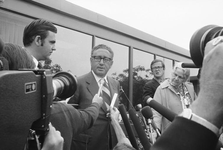 A man in spectacles speaks into a microphone.