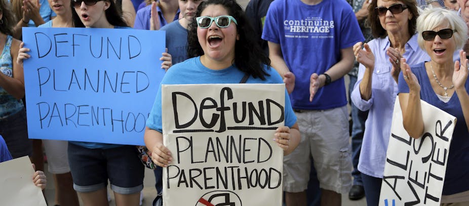 A group of people hold up signs saying 'Defund Planned Parenthood'