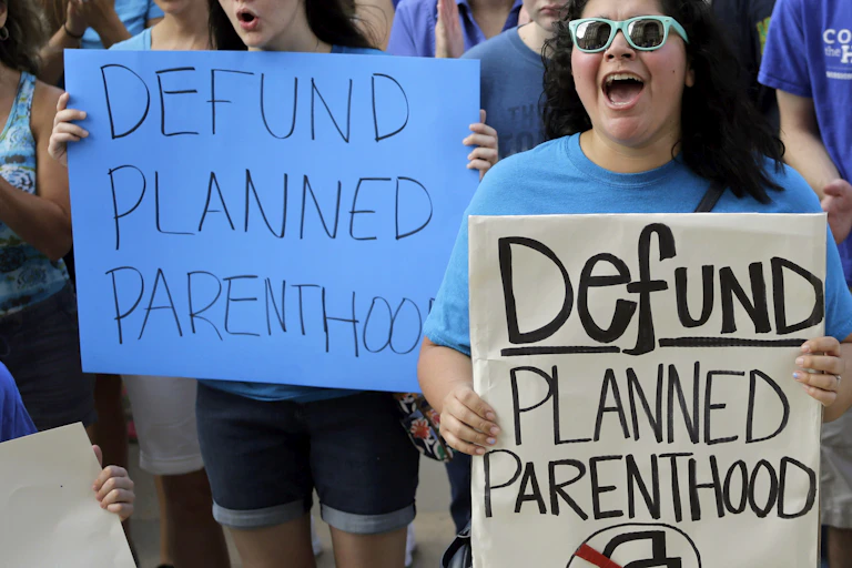 A group of people hold up signs saying 'Defund Planned Parenthood'