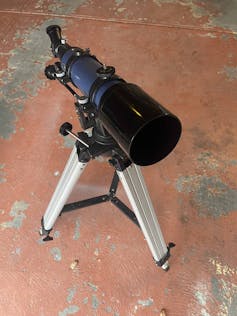 A small telescope is placed on a simple stand on a concrete floor