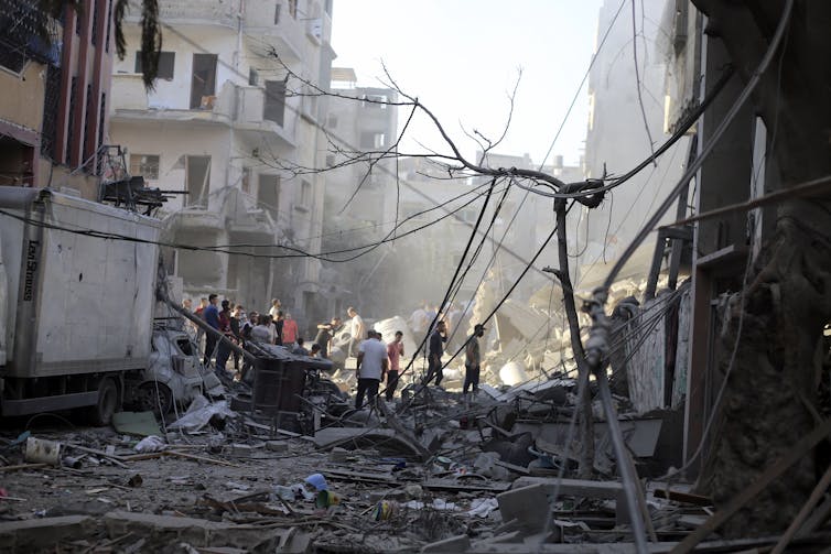 People walk among debris from heavily damaged buildings.