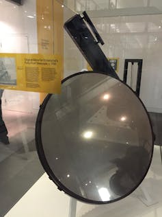 A circular mirror behind a glass screen in a museum