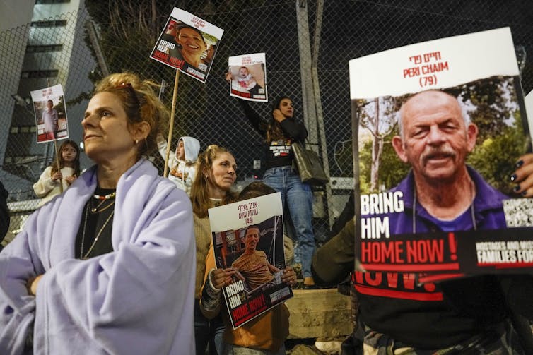 Protestors marching with placards that have photographs of individuals with 'Bring her home,' or 'Bring him home,' written at the bottom.