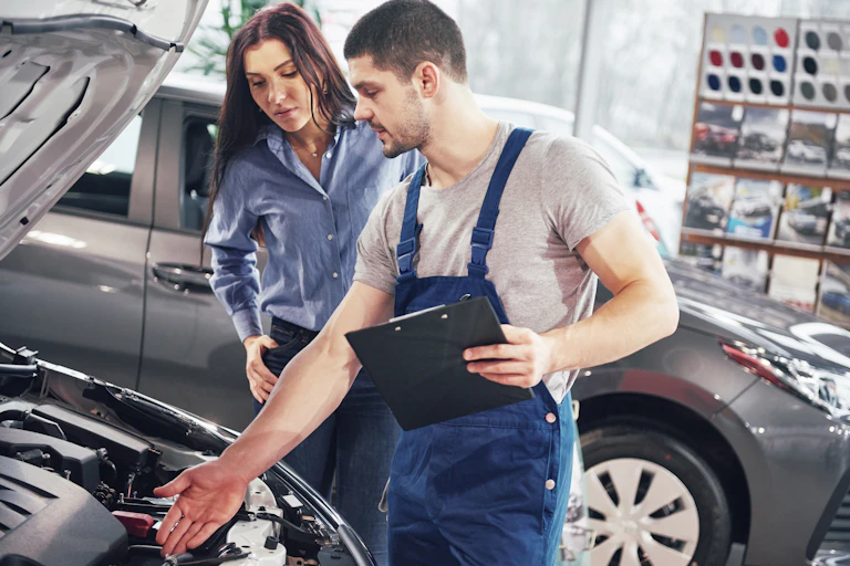 Male mechanic and woman standing in front of an open car hood