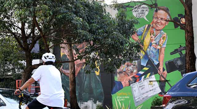A cyclist rides past a mural depciting Scott Morrison.