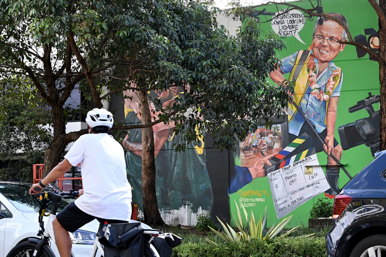 A cyclist rides past a mural depciting Scott Morrison.