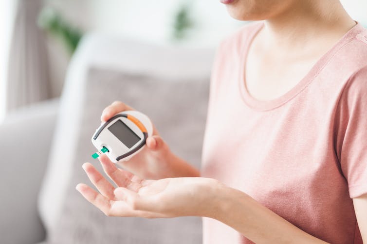 Woman sitting on sofa, taking finger prick test for blood sugar levels