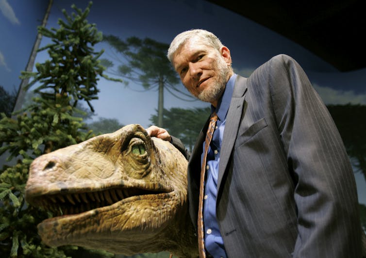 Man in a grey jacket poses with a replica dinosaur.