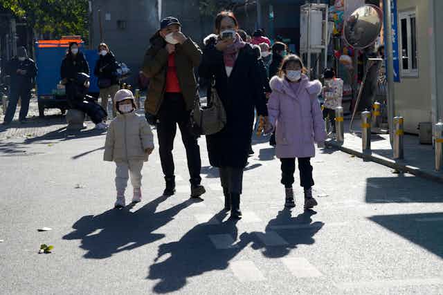 Dos adultos y dos niños caminan por Pekín con máscaras.