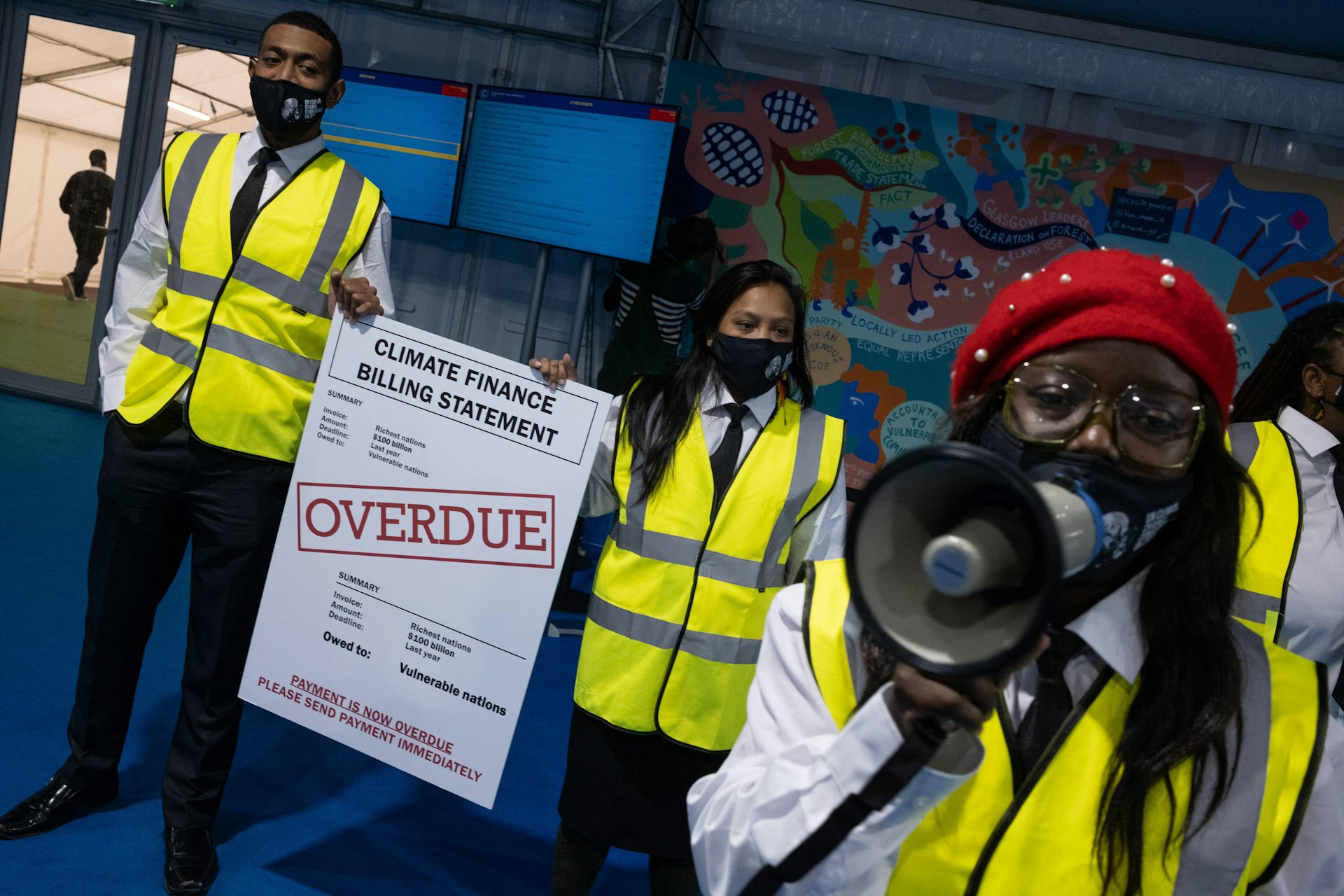 Three people in hi-vis vests holding an 'climate finance overdue' statement.