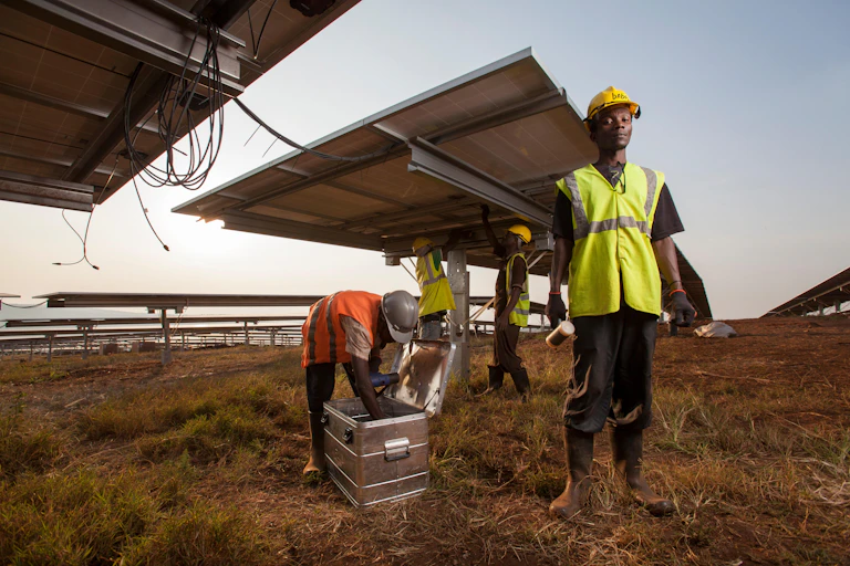 Engineers stand under rows of solar panels.