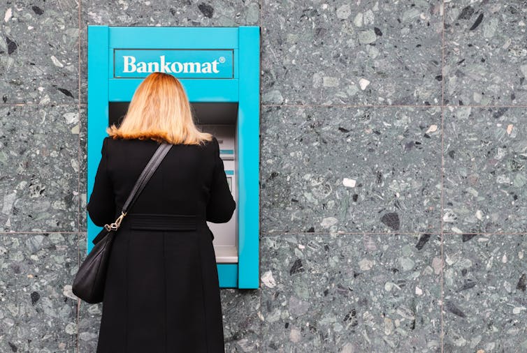View of the back of a well-dressed woman at an in-wall cash machine, with the word Bankomat at the top
