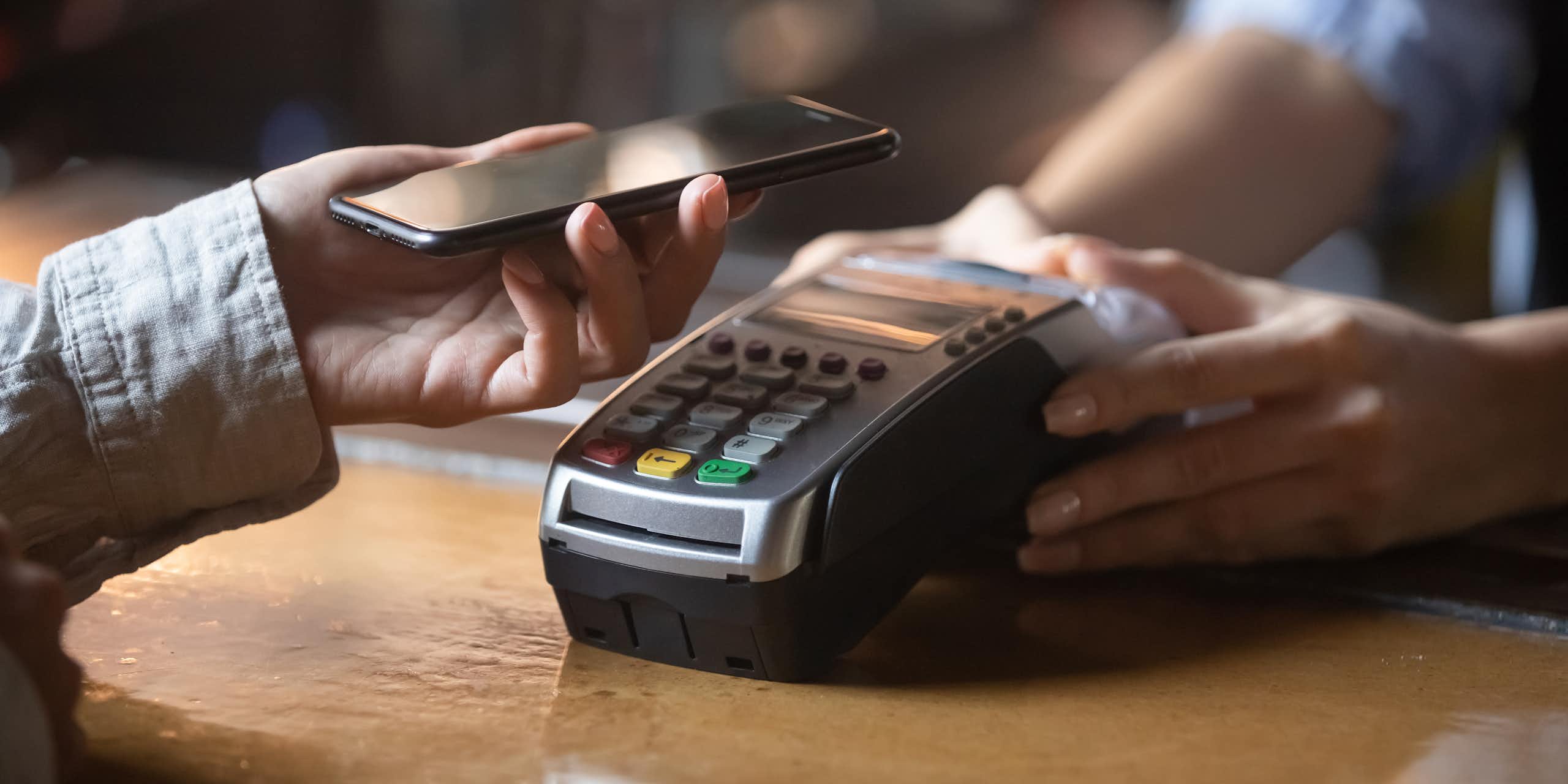 Close up of a hand using a mobile phone to pay on a contactless card machine