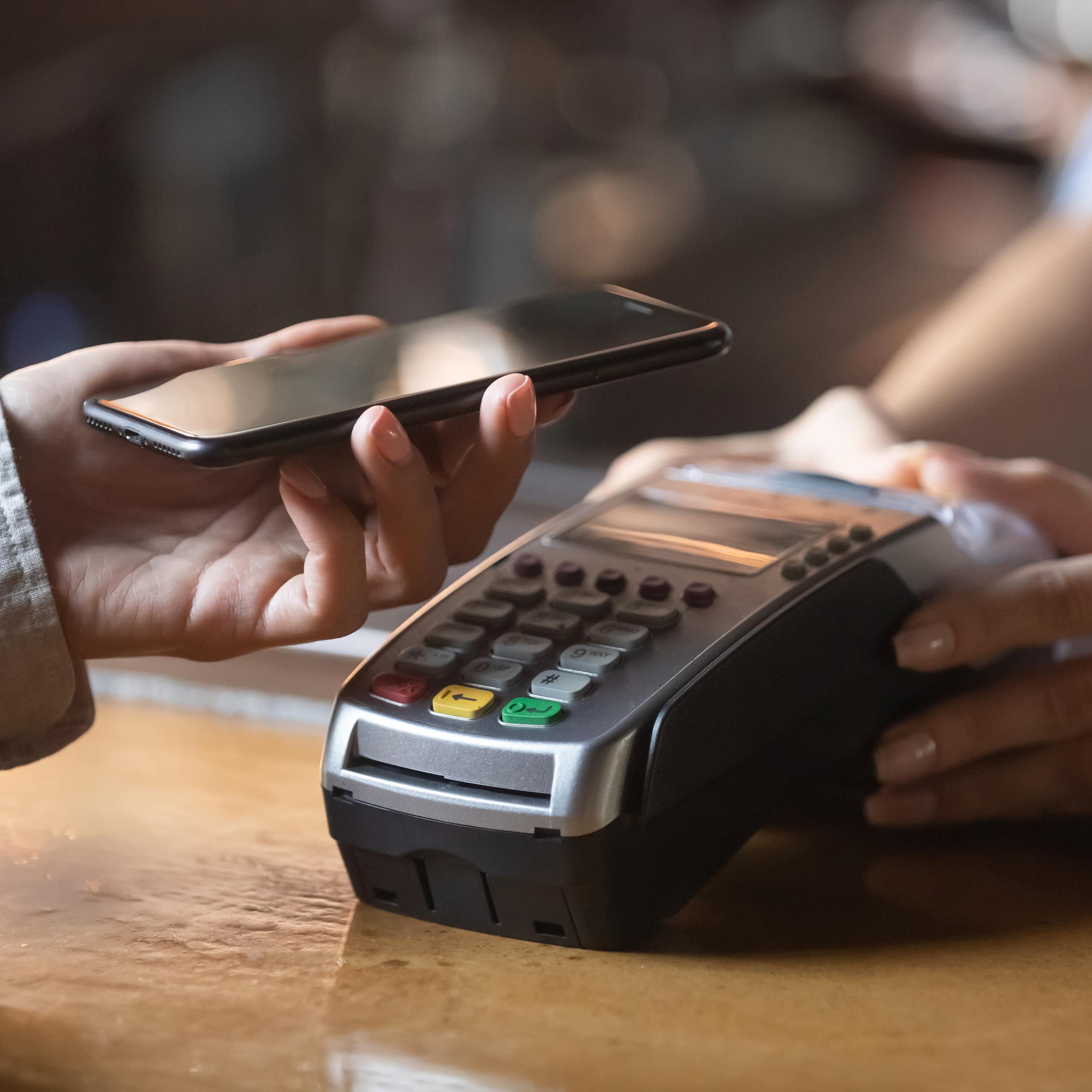 Close up of a hand using a mobile phone to pay on a contactless card machine