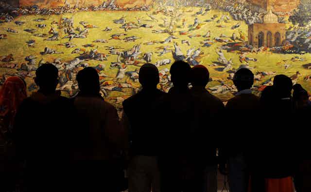 A group in shadow look at a painting depicting a massacre.