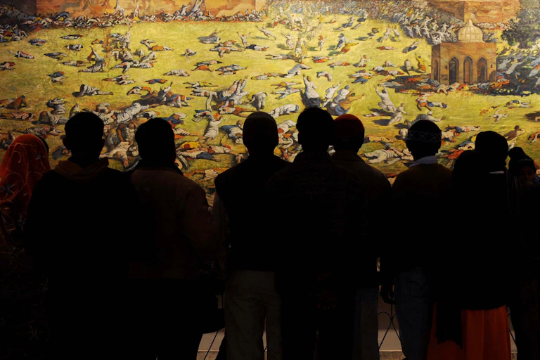 A group in shadow look at a painting depicting a massacre.