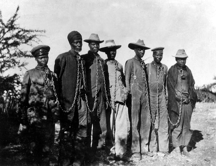 A group of men stand with chains around their necks