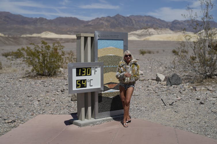 Una mujer con abrigo frente a un termómetro en el desierto.
