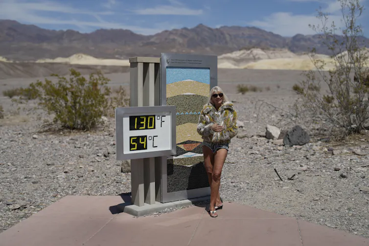 A woman wearing a coat seen against a thermometer in the desert.