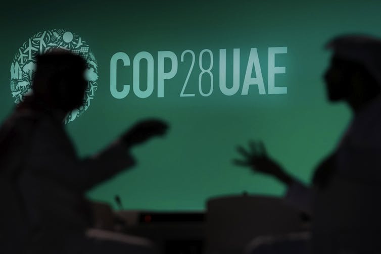 People are silhouetted against a logo for the COP28 U.N. Climate Summit
