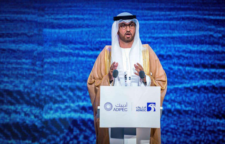 A man in traditional Arab robes at a podium.