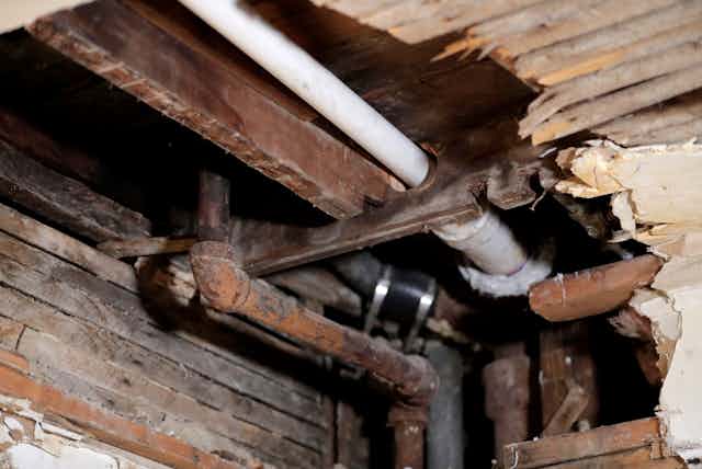 Pipes are visible through a hole in the ceiling of an older home.