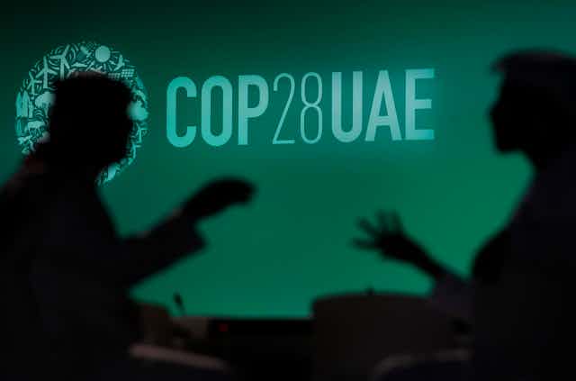 Two people are silhouetted against a logo for the COP28 U.N. Climate Summit, Nov. 29, 2023, in Dubai, United Arab Emirates