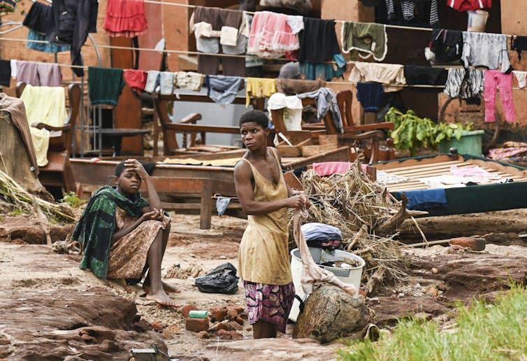 Two women wash clothes in a bucket in the year as they clean up from the storm's damage.