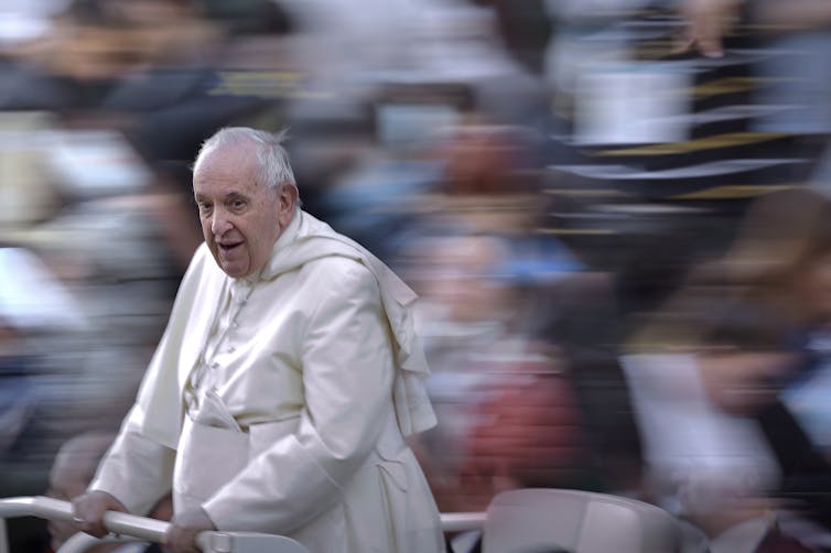Pope Francis holding on to a railing as he greets people.