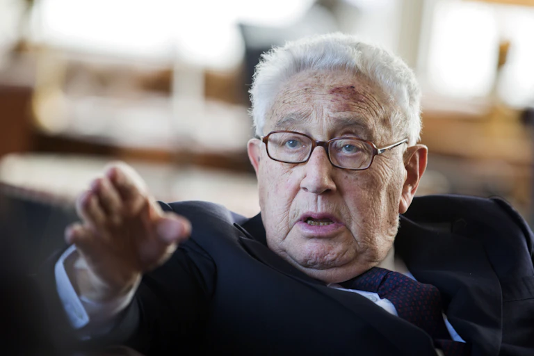 A grey-haired man points past a camera