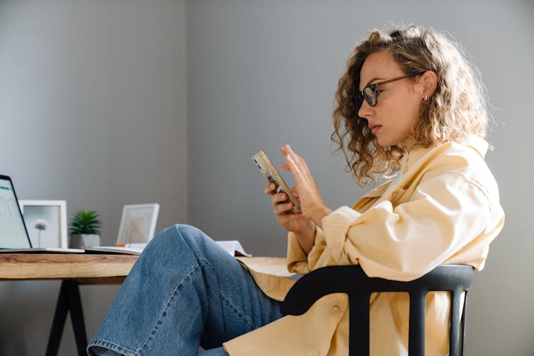 A woman looks at her phone while sitting in a chair.