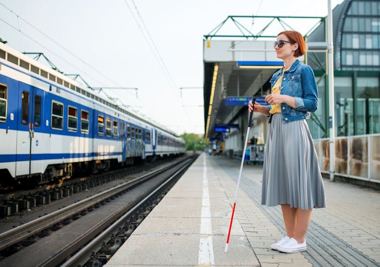 Portrait of blind woman with white cane standing on train station outdoors in city