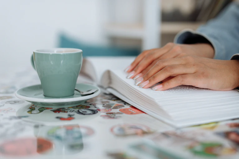 a woman's hands reading a braille book, alongside a cup and saucer