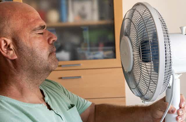 Man closes eyes, facing a fan