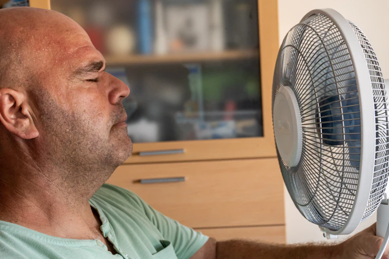 Man closes eyes, facing a fan