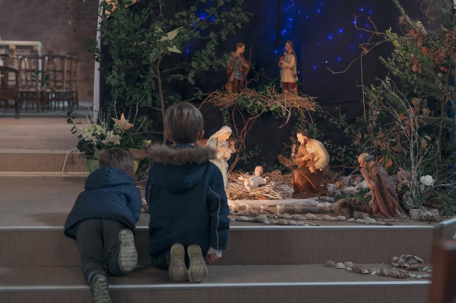 Two children kneel in front of a nativity display.