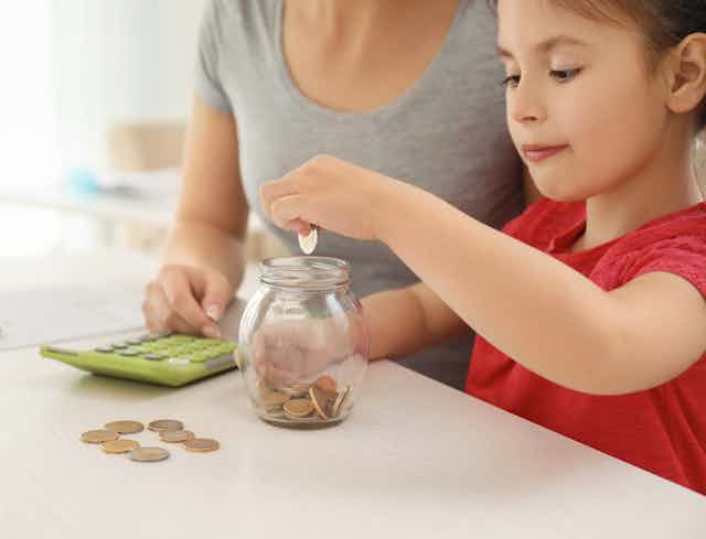 Little girl with her mother sitting at a table and counting coins.