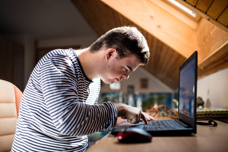 A young man with Down's syndrome types on a laptop.